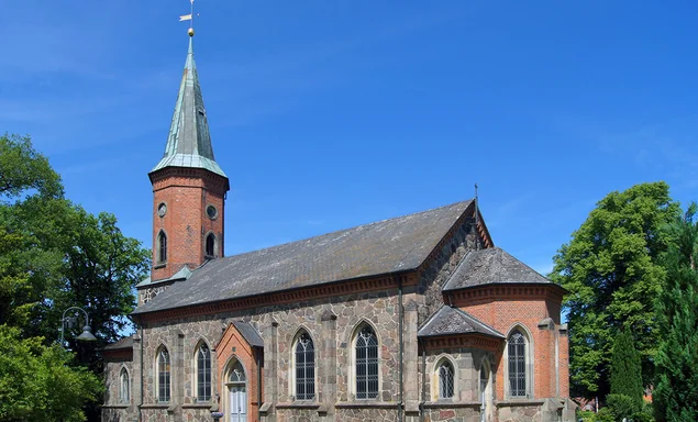 Kirche von rechts, vorn 2 Steige und Laterne links, grüne Eichen beidseitig, im Hintergrund rechts Gutsscheune